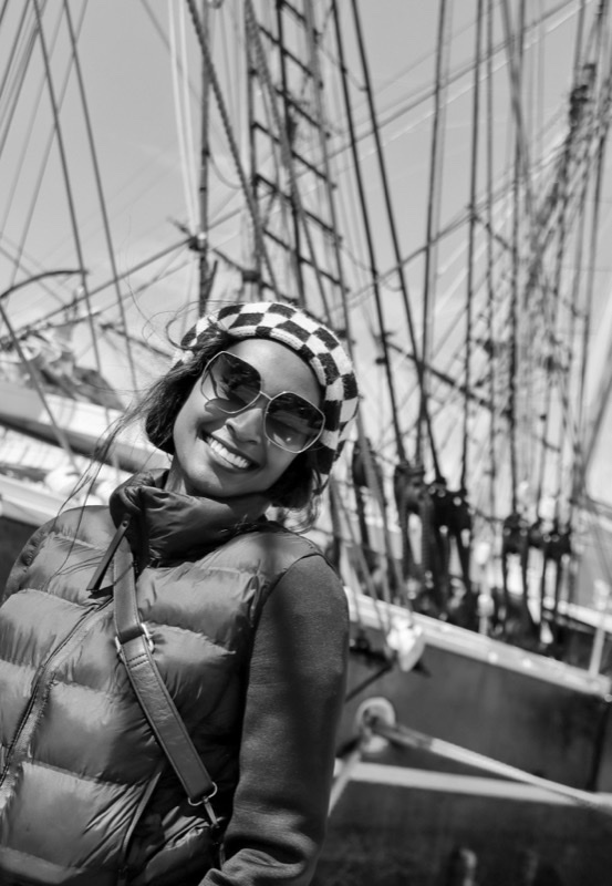 Alice on the deck of a tall ship, smiling in sunglasses and a patterned beanie.