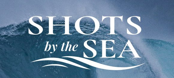 Shots by the Sea wordmark set over a breaking wave